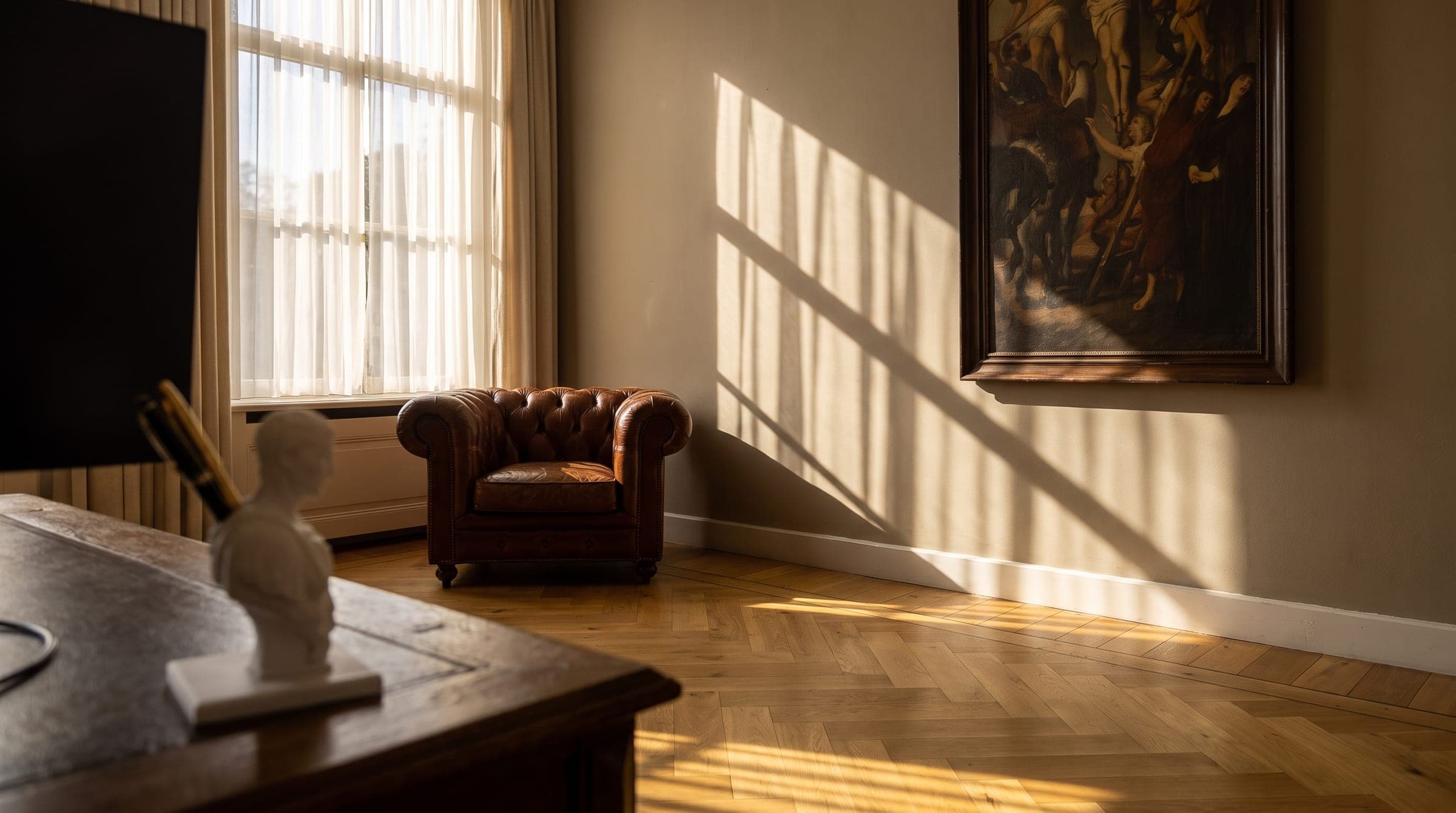 Licht en schaduwbanen vallen door een hoog venster over een lege fauteuil